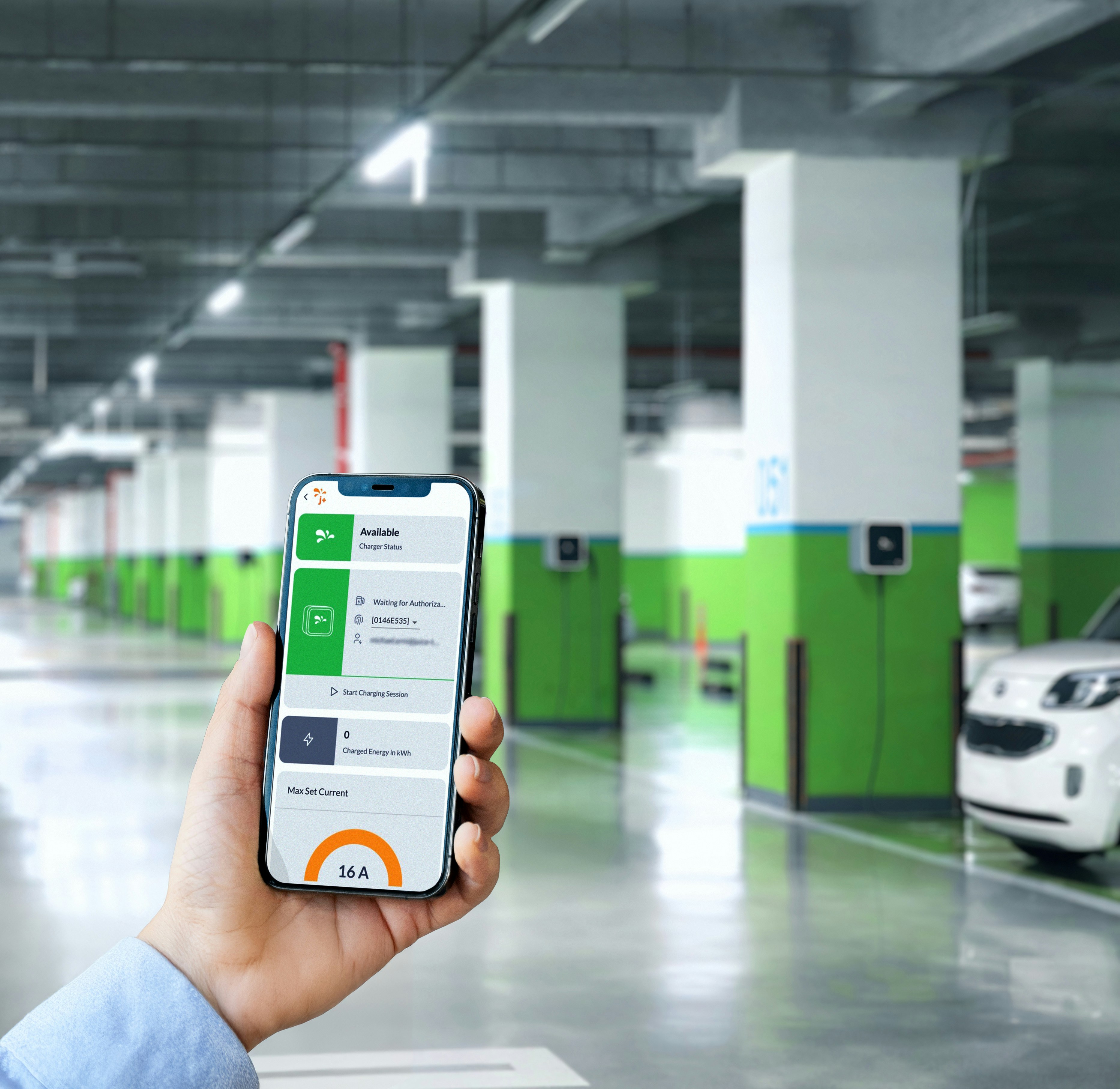 Person holding smartphone with EV charging app interface in a parking garage with charging stations